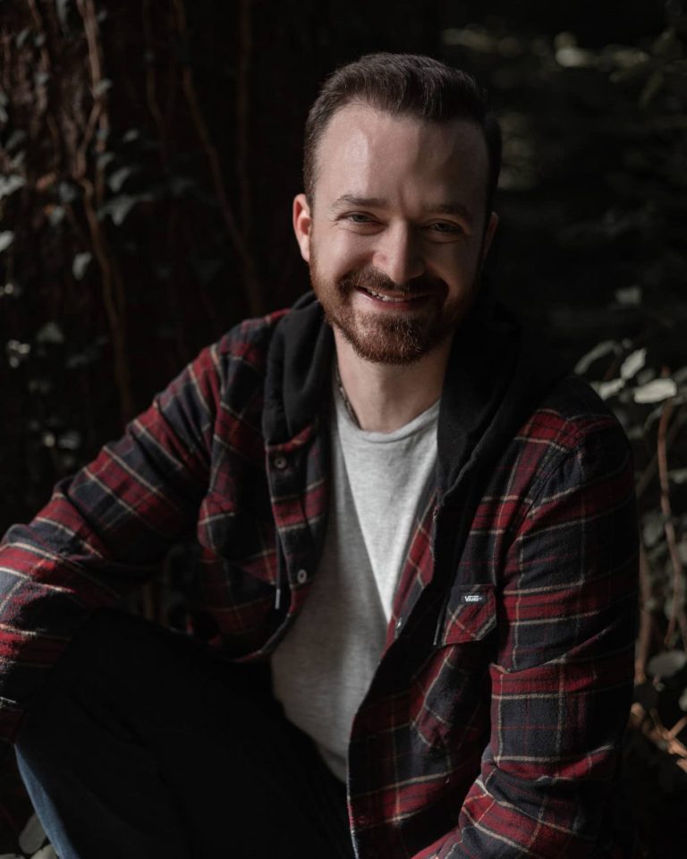 Lachendes Porrait von einem jungen Mann mit rotem Hemd vor einem Baum